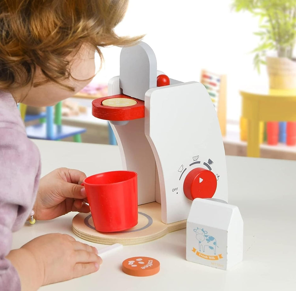 Child playing with a toy coffee maker and cup on a table.